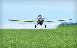 Airplane spraying herbicide onto field.